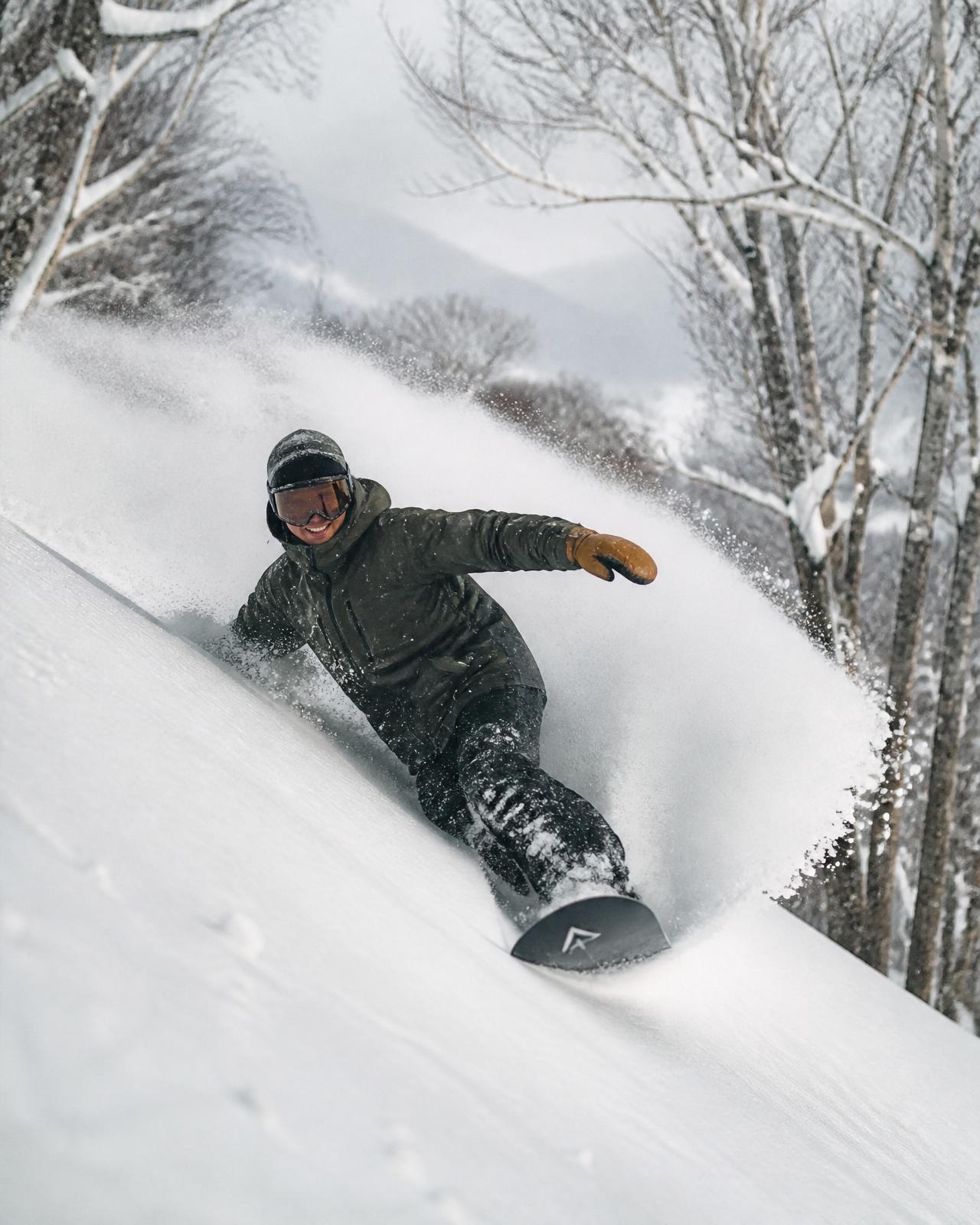 A snowboarder carving fresh powder through the trees